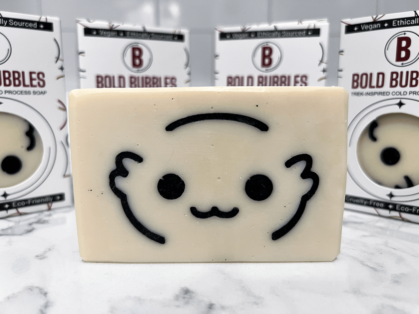 A white bar of soap with the outlines of a cute creature's face called a Moopsy in black. The design was inspired by the adorable but deadly creature from Star Trek: Lower Decks. This soap comes in a variety of scents.