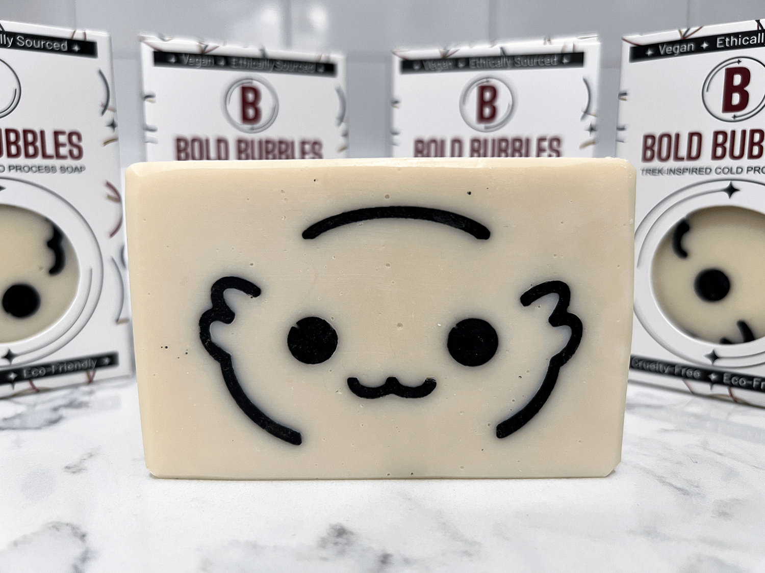 A white bar of soap with the outlines of a cute creature's face called a Moopsy in black. The design was inspired by the adorable but deadly creature from Star Trek: Lower Decks. This soap comes in a variety of scents.